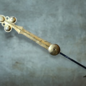 May include: A gold-colored clock hand with a decorative, ornate tip and a black metal rod.