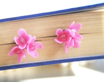 May include: A pair of pink flower-shaped earrings. The earrings are made of polymer clay and have a delicate, feminine look.
