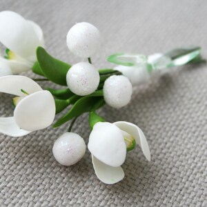 May include: A white flower bouquet with green leaves and white sparkly beads. The bouquet is made of artificial flowers and is ideal for a wedding or other special occasion.
