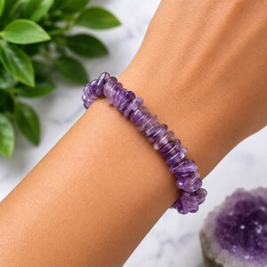 May include: A bracelet composed of numerous small, polished, translucent purple amethyst beads in a disc shape. The beads are strung together in a continuous circular pattern, showcasing varying shades of deep violet and light lavender throughout.