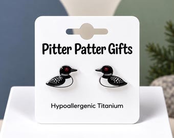 Könnte beinhalten: Ein Paar Ohrstecker in Form von Eistauchern mit schwarz-weißem Gefieder und roten Augen. Die Ohrringe sind auf einer weißen Präsentationskarte befestigt, die mit Pitter Patter Gifts und Hypoallergenic Titanium beschriftet ist.