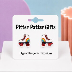 May include: A pair of white roller skate earrings with red laces, red wheels, and a rainbow graphic on the side. The earrings are attached to a white display card labeled Pitter Patter Gifts and Hypoallergenic Titanium in black text.