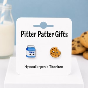 May include: A pair of stud earrings featuring a blue and white milk carton and a brown chocolate chip cookie, both with smiling faces. The earrings are displayed on a white card labeled Pitter Patter Gifts and Hypoallergenic Titanium.