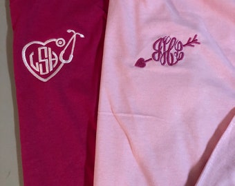 May include: Two long-sleeved shirts, one pink and one burgundy, with embroidered monograms. The pink shirt has a heart with an arrow through it and the monogram "JFF". The burgundy shirt has a heart with a stethoscope and the monogram "LSH".