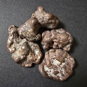 May include: Four irregularly shaped pieces of raw copper metal. The copper is a reddish-brown color and has a rough, textured surface.