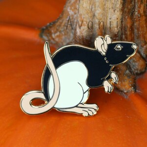 Op de afbeelding: Een zwarte en witte emaille pin van een rat met een gouden rand. De rat zit op een pompoen.