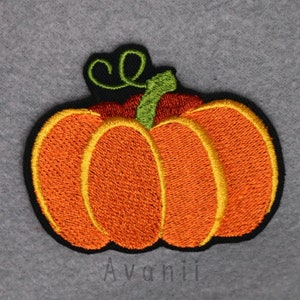 Può includere: Un toppa di zucca arancione ricamata con un gambo verde e una foglia arricciata. La zucca è bordata di nero e ha un contorno giallo attorno al centro.