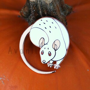 Op de afbeelding: Een witte emaille pin van een cartoonmuis met een roségouden rand. De muis is opgerold in een cirkel met zijn staart om zijn lichaam gewikkeld. De muis heeft zwarte ogen en een roze neus.