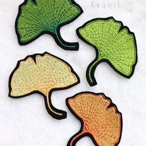 Op de afbeelding: Vier geborduurde ginkgo-bladpatches in verschillende kleuren: groen, geel en oranje. De patches zijn allemaal even groot en hebben dezelfde vorm en een eenvoudig, elegant ontwerp.