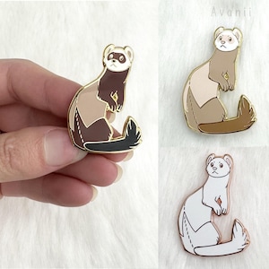 Puede incluir: Tres pines de esmalte con un hurón de dibujos animados en diferentes poses. El hurón es marrón y blanco con una cola larga y delgada. Los pines son de color dorado y tienen un acabado brillante.