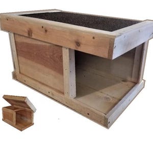 May include: A rectangular wooden pet shelter featuring a natural light brown wood grain finish, a flat roof covered with a dark textured material, and an open side entrance. The structure is built with visible wooden planks and metal fasteners.