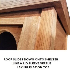 May include: Close-up of a wooden birdhouse with a hinged roof that slides down to cover the opening. The roof is made of natural wood with a light brown color. The text "ROOF SLIDES DOWN ONTO SHELTER LIKE A LID SLEEVE VERSUS LAYING FLAT ON TOP" is printed below the image.