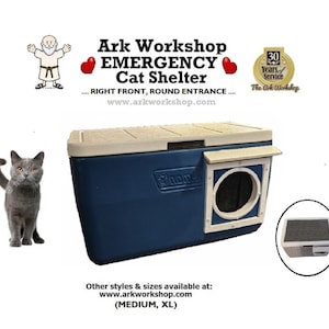 May include: A blue and beige emergency cat shelter with a round entrance. The shelter has the text "Ark Workshop EMERGENCY Cat Shelter" and "www.arkworkshop.com". A gray cat is standing to the left of the shelter.