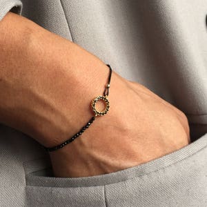 May include: A black string bracelet with a gold circle charm set with black stones.