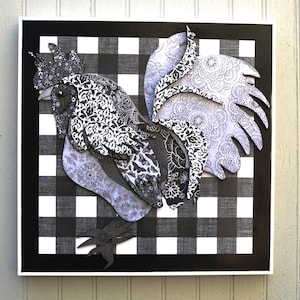 May include: A layered paper rooster art piece. The rooster is primarily black and white, with intricate patterns and textures. It is set against a black and white checkered background, framed in black and white.