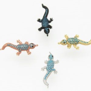 May include: Four lizard charms with blue crystal accents. The lizards are in different colors: black, gold, rose gold, and silver.