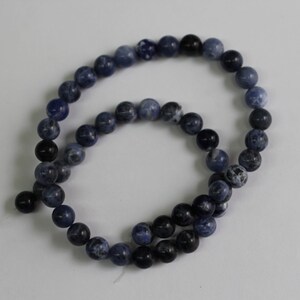 May include: A strand of blue and black gemstone beads. The beads are round and have a smooth, polished finish.