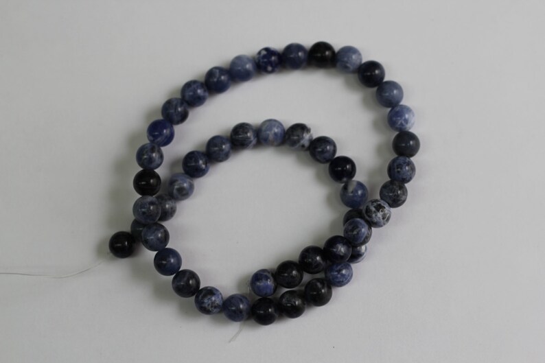 May include: A strand of blue and black gemstone beads. The beads are round and have a smooth, polished finish.
