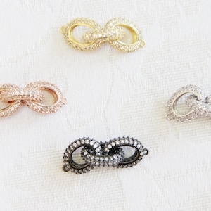 May include: Four different colored metal clasps with clear crystal embellishments. The clasps are in gold, rose gold, silver, and black.