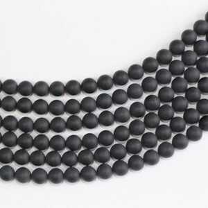 May include: A strand of black matte round beads, arranged in a curved pattern on a white surface.
