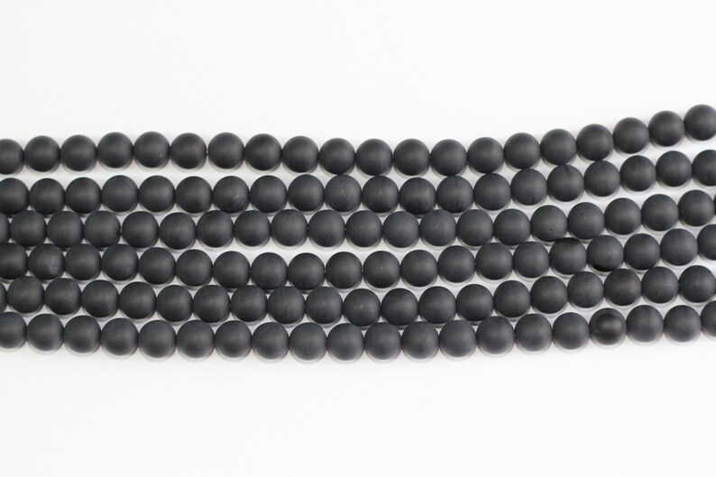 May include: A strand of black matte round beads. The beads are uniform in size and shape, and they are strung together on a clear thread.