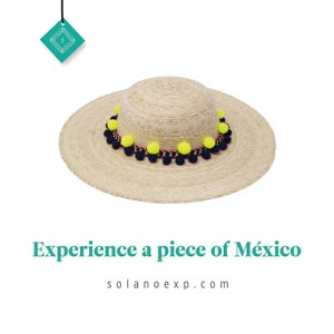 May include: A wide-brimmed straw hat with a black and pink trim and yellow pom-poms. The hat is made in Mexico. Experience a piece of México. solanoexp.com