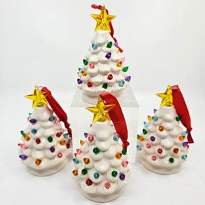 May include: Four white ceramic Christmas tree ornaments with textured branches, each decorated with small multicolored light bulbs and topped with a translucent yellow star. A red ribbon loop is attached to the top of each tree for hanging.