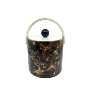 May include: A vintage ice bucket with a white lid and handle, and a black knob. The bucket has a mottled pattern in shades of brown, black, and gold. The handle is arched and cream-coloured.