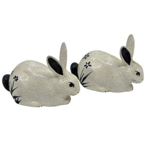 May include: Two ceramic rabbit figurines. The rabbits are white with black accents on the ears and tail. They are decorated with black floral designs. The ceramic has a crackle glaze finish.