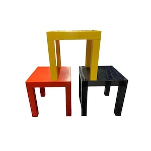 May include: Three small square tables in primary colors: red, yellow, and black. The yellow table is stacked on top of the red table, and the black table is next to the red table. The tables have a simple, modern design.