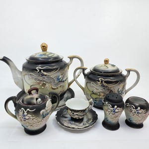 Op de afbeelding: Een complete zwart-witte porseleinen theeset met drakenmotieven. De set bevat twee theepotten, een suikerpot, een kop en schotel, een zoutvaatje en een kleine vaas. Gouden accenten en gedetailleerde drakenontwerpen sieren elk stuk.