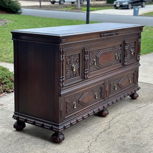May include: A dark brown wooden chest featuring a rectangular top, a hinged lid, and a front panel adorned with intricate carved geometric patterns and floral motifs. The piece includes brass drop pulls and rests on four carved ball and claw feet.
