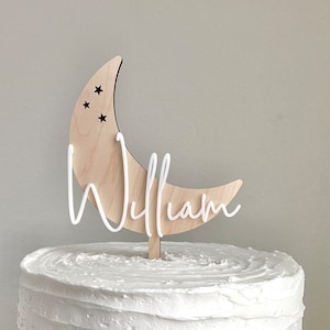 May include: A wooden crescent moon cake topper with three small stars and the name "William" written in white script.