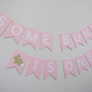 May include: Pink and white banner with the text "Some Bunny Is One" and gold glitter bunny silhouettes.