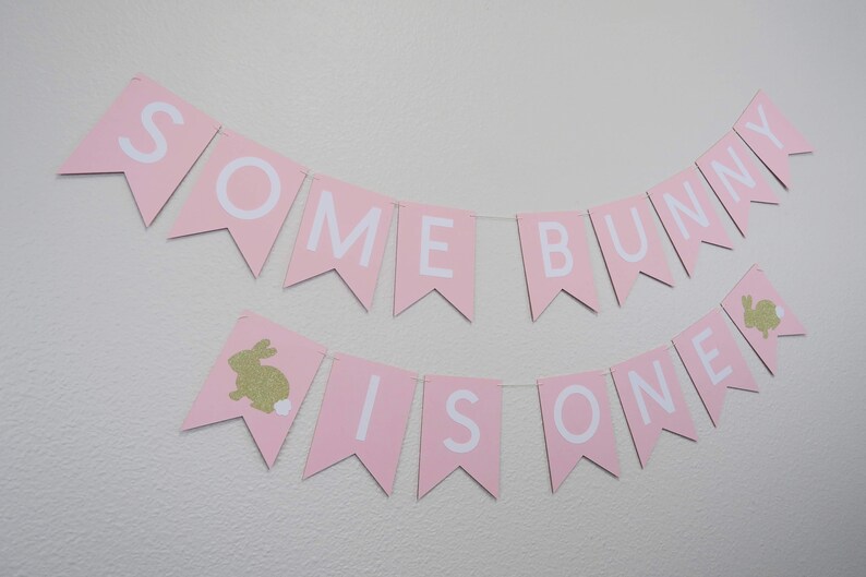 May include: Pink and white banner with the text "Some Bunny Is One" and gold glitter bunny silhouettes.