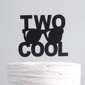 May include: Black cake topper with the text "TWO COOL" and a pair of sunglasses.