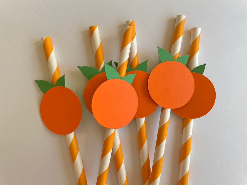 Peut inclure: Six pailles en papier ray&eacute;es orange et blanc avec des cercles en papier orange attach&eacute;s au sommet. Chaque cercle a des feuilles en papier vert attach&eacute;es sur le c&ocirc;t&eacute;.