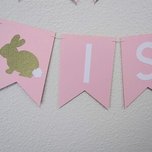 May include: Pink and white banner with the word "It's" and a gold glitter bunny with a white tail.