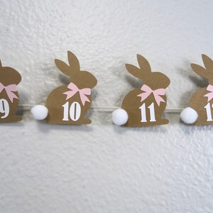 May include: A brown paper bunny garland with pink bows and white pom-poms. The bunnies are numbered 9, 10, 11, and 12.