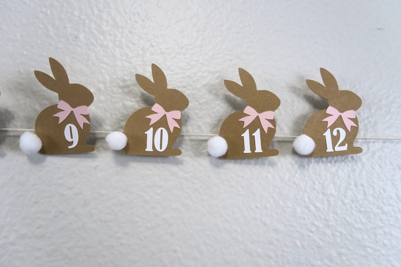 May include: A brown paper bunny garland with pink bows and white pom-poms. The bunnies are numbered 9, 10, 11, and 12.