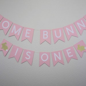 May include: Pink banner with white letters that reads "Some Bunny Is One" with gold glitter bunny silhouettes on each end.