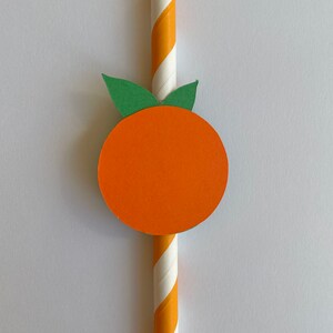 Peut inclure: Une paille en papier ray&eacute;e de blanc et d'orange avec une feuille verte et un cercle orange attach&eacute;s au sommet, ressemblant &agrave; une orange.