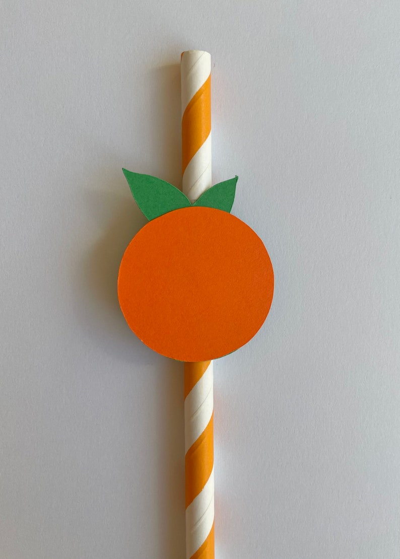 Peut inclure: Une paille en papier ray&eacute;e de blanc et d'orange avec une feuille verte et un cercle orange attach&eacute;s au sommet, ressemblant &agrave; une orange.