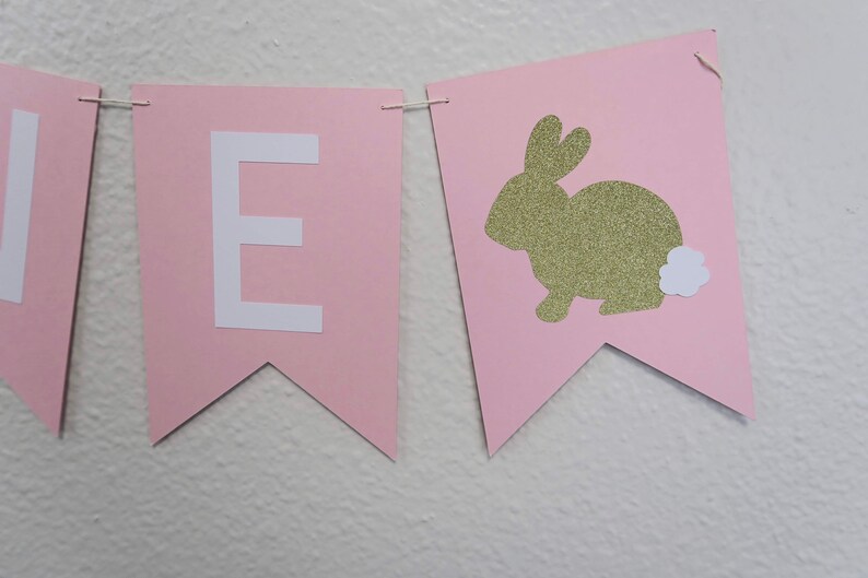 May include: Pink and white banner with the letter "E" and a gold glitter bunny with a white fluffy tail.