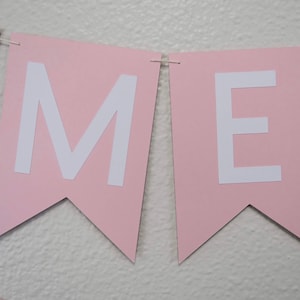 May include: Pink banner with the letters "OME" in white. The banner is made of paper and has a scalloped edge.