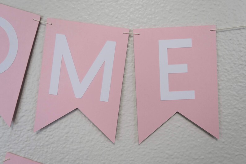 May include: Pink banner with the letters "OME" in white. The banner is made of paper and has a scalloped edge.