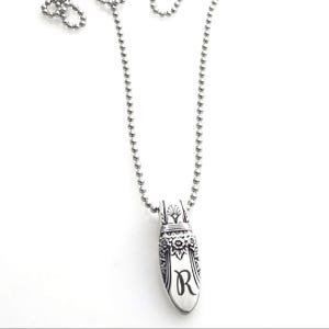 May include: Silver-toned pendant necklace with a ball chain. The pendant is elongated with floral and decorative details, and the letter "R" is engraved on the front. The necklace is displayed against a white background.