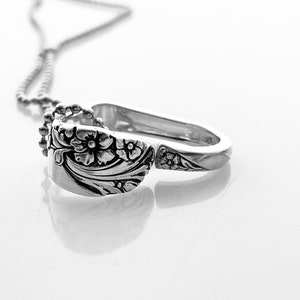 May include: A silver necklace with a pendant made from a spoon with a floral design.