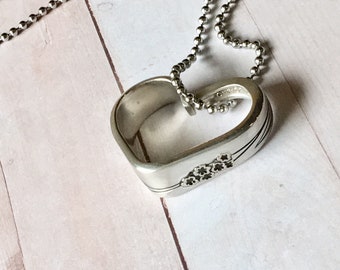 May include: A silver heart-shaped pendant necklace with a delicate ball chain. The pendant is made from a spoon with a floral design.