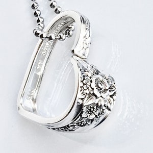 May include: A silver heart-shaped pendant necklace. The pendant is crafted from a repurposed spoon, featuring floral detailing on the heart's lower portion. The necklace has a delicate ball chain.